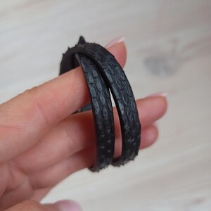 May include: Two black leather bracelets with a textured pattern. The bracelets are stacked on top of each other.