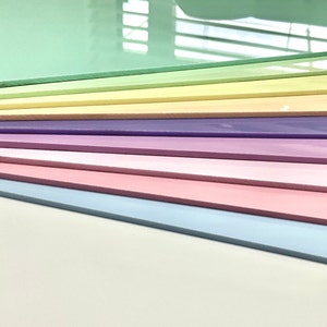 May include: A collection of pastel-colored rectangular sheets, arranged in a layered pattern. The colors include shades of green, yellow, purple, pink, and blue. The sheets appear to be made of a smooth, glossy material, with a white surface in the foreground.