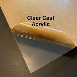 May include: A clear sheet of acrylic plastic with a brown paper backing. The text "Clear Cast Acrylic" is printed on the paper.