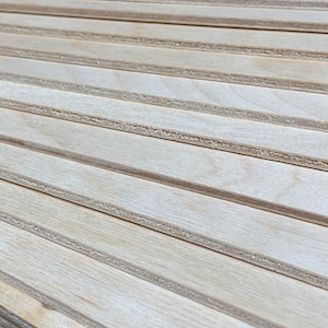 K&ouml;nnte beinhalten: Ein Stapel d&uuml;nner, heller Holzplatten mit einer glatten, nat&uuml;rlichen Oberfl&auml;che. Die Platten sind versetzt gestapelt und erzeugen so eine optische Textur.