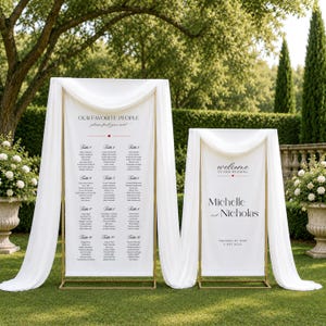 Puede incluir: Dos carteles de boda verticales de tela blanca sobre soportes de metal dorado drapeados con gasa blanca. El cartel izquierdo dice OUR FAVORITE PEOPLE y enumera las mesas del 1 al 12. El cartel derecho dice welcome TO OUR WEDDING Michelle and Nicholas.