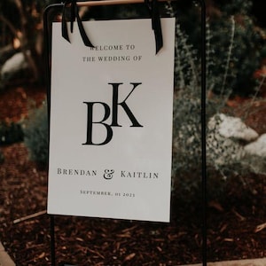 May include: A white wedding sign with black text and a black and white monogram. The sign reads "Welcome to the wedding of BK Brendan & Kaitlin September, 01 2023".