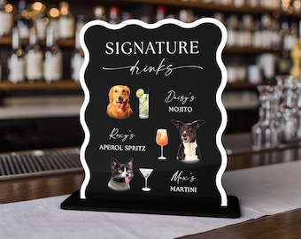 May include: A black, wavy-edged sign with white text reading SIGNATURE drinks, Daisy's MOJITO, Roxy's APEROL SPRITZ, and Max's MARTINI. The sign features illustrations of a golden retriever, a black and white dog, a cat, and three cocktails.