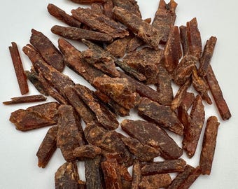 May include: A collection of raw, elongated crystal shards in varying shades of deep reddish-brown and burnt orange. These natural mineral fragments feature jagged, uneven edges and a translucent, fibrous texture throughout the scattered pile.