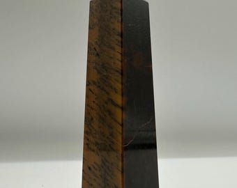 May include: A polished stone tower with a pointed top, featuring a vertical orientation. The surface displays a mix of dark brown and golden-brown bands with natural linear patterns, creating a distinct contrast between the light and dark sections.