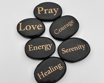 May include: Six black smooth stones with gold lettering. The words on the stones are "Pray", "Love", "Courage", "Energy", "Serenity", and "Healing".
