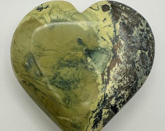 May include: A heart-shaped stone featuring a smooth, polished surface with a marbled pattern. The colors include shades of light olive green, dark forest green, and deep brown, with intricate natural veining throughout the entire object.