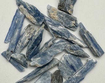 May include: A collection of raw kyanite crystal blades featuring elongated, bladed structures with a distinct blue coloration, interspersed with white and grey mineral inclusions, showcasing a natural, fibrous, and layered crystalline texture.