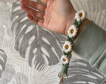 May include: A green and white crocheted keychain with a gold metal clasp. The keychain is decorated with white daisy flowers with yellow centers.