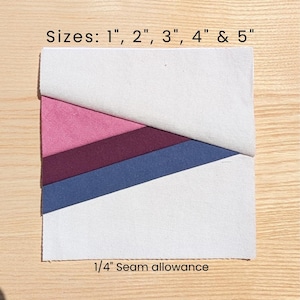 May include: A square fabric piece with diagonal sections in white, pink, burgundy, and blue. The text "Sizes: 1", 2", 3", 4" & 5"" and "1/4" Seam allowance" is printed on the image. The fabric is on a light wood surface.