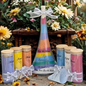 May include: A clear glass unity sand ceremony set featuring a large central cone-shaped bottle and several smaller cylindrical bottles, all filled with layered coloured sand. Each bottle is topped with a wooden cork and a white ribbon bow.