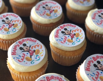 Puede incluir: Primer plano de cupcakes decorados con imágenes comestibles redondas de Mickey Mouse. Los cupcakes están cubiertos con glaseado blanco y tienen las palabras "Happy Birthday" en las imágenes.