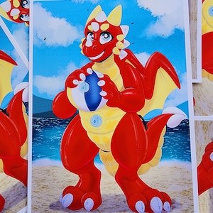 May include: A red inflatable dragon with yellow accents holds a blue beach ball. The dragon has a friendly expression and is standing on a sandy beach with blue water in the background.
