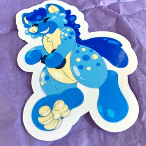 May include: A blue and yellow cartoon animal sticker with a happy expression. The animal has a spotted pattern and a large tail.