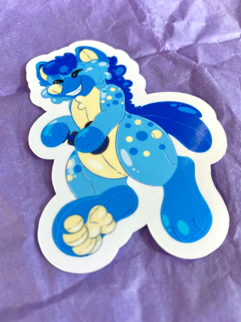 May include: A blue and yellow cartoon animal sticker with a happy expression. The animal has a spotted pattern and a large tail.
