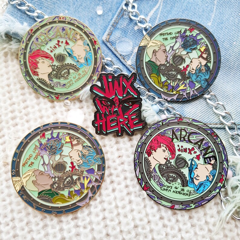 May include: Five enamel pins featuring characters from the animated series Arcane. The pins are circular and feature a green, blue, and purple color scheme. The text on the pins reads "Arcane" and "Jinx".