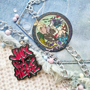 May include: Two enamel pins on a denim background. One pin is round and features a colorful illustration of two people with the text "Pretend Like The First Time". The other pin is red and black and features the text "I'm Not Here".
