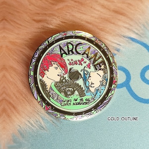 May include: Gold-colored pin with a circular design featuring two female characters from the show Arcane. The characters are Jinx and Vi. The pin has a green, purple, and black color scheme with the words "Arcane" and "Jinx" written on it. The text "Everybody wants to be in my crew" is written in a circle around the characters.
