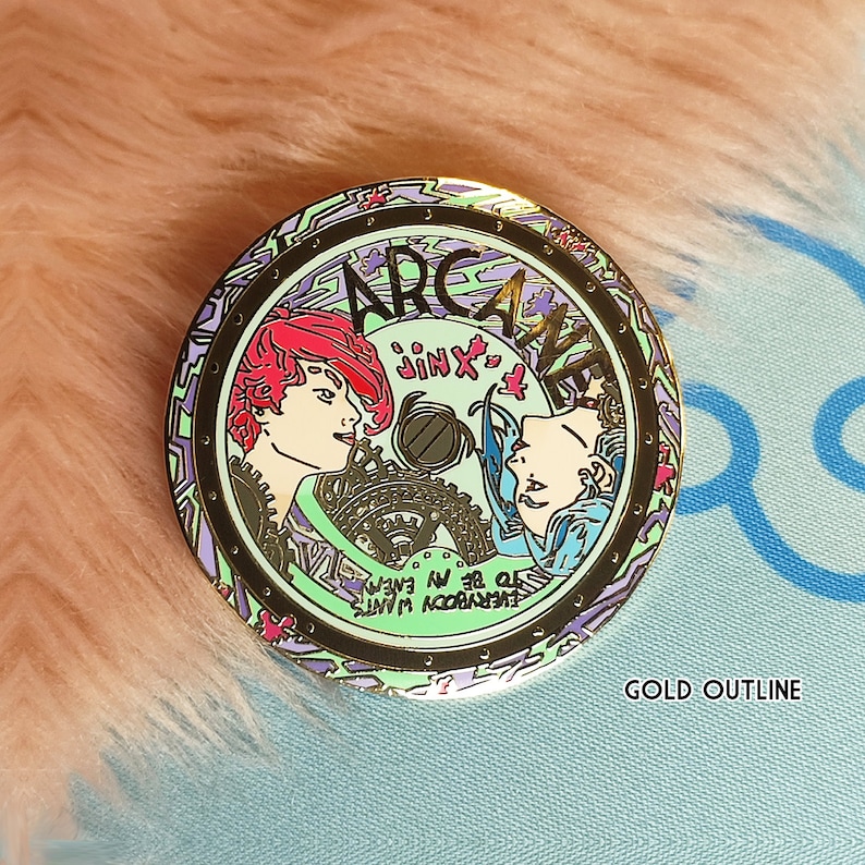 May include: Gold-colored pin with a circular design featuring two female characters from the show Arcane. The characters are Jinx and Vi. The pin has a green, purple, and black color scheme with the words "Arcane" and "Jinx" written on it. The text "Everybody wants to be in my crew" is written in a circle around the characters.