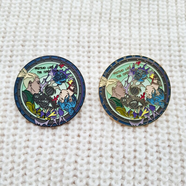 May include: Two gold-toned enamel pins with a blue, green, and purple color scheme. The pins feature a circular design with a stylized image of two people with the text "Pretend Like The First Time" in a white font.