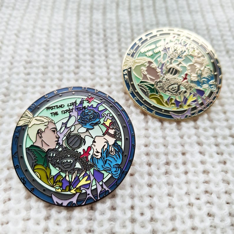 May include: Two round enamel pins with a gold finish. The first pin features a colorful illustration of two people with the text "Pretend Like The First Time". The second pin features a colorful illustration of a circle with a floral design.