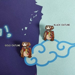 May include: Two enamel pins of a cartoon robot monkey holding a banana. One pin has a black outline and the other has a gold outline.