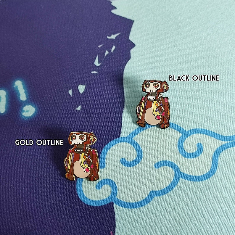 May include: Two enamel pins of a cartoon robot monkey holding a banana. One pin has a black outline and the other has a gold outline.