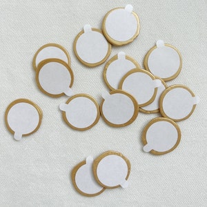 May include: A collection of 14 gold-rimmed, round, adhesive stickers with white centers. The stickers are arranged in a random pattern on a white surface.