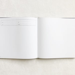 May include: An open blank book with a black cover. The book is lying flat on a white surface.
