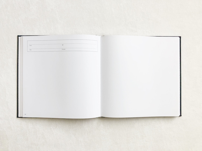 May include: An open blank book with a black cover. The book is lying flat on a white surface.