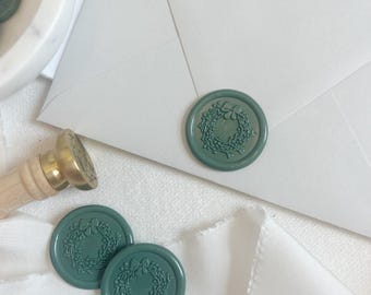 May include: Three green wax seals with a wreath design. The seals are on a white surface.