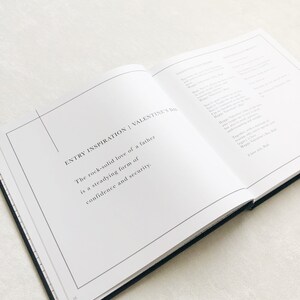 May include: An open book with a white background and black text. The text reads "ENTRY INSPIRATION | VALENTINE'S DAY" and "The rock-solid love of a father is a steadying form of confidence and security."