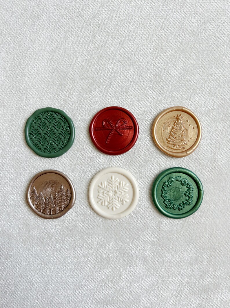 May include: Six round wax seals with different holiday designs. The seals are in various colors, including green, red, gold, and white. The designs include a snowflake, a Christmas tree, a wreath, a bow, a forest, and a pine tree.