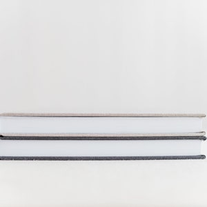 May include: Two hardcover books stacked on top of each other. The top book has a light brown cover and the bottom book has a dark gray cover.