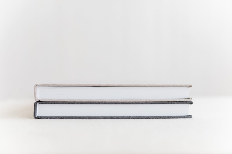 May include: Two hardcover books stacked on top of each other. The top book has a light brown cover and the bottom book has a dark gray cover.