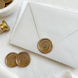 Op de afbeelding: Gouden waszegels met een honingraatontwerp op een witte achtergrond. De zegels worden gebruikt om enveloppen te versieren en een vleugje elegantie toe te voegen aan correspondentie.