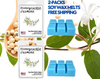 May include: Two packs of Honeysuckle Jasmine soy wax melts in blue cubes. The wax melts are packaged in white boxes with a floral design and the text "Honeysuckle Jasmine" printed on them. The image also includes a wooden spoon filled with soy beans and a honeysuckle vine with white flowers.