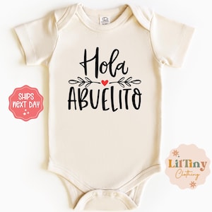 May include: A beige baby onesie with black text that reads "Hola Abuelito" with a red heart and leafy branches.