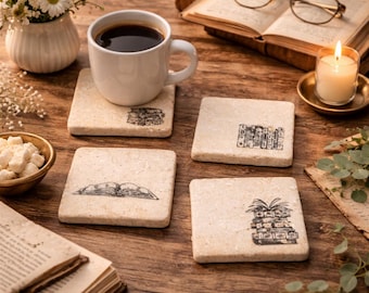 May include: A white coffee mug filled with dark coffee sits on a square stone coaster with a book illustration. The image features three other coasters with book designs, a lit candle, and an open book on a wooden surface.