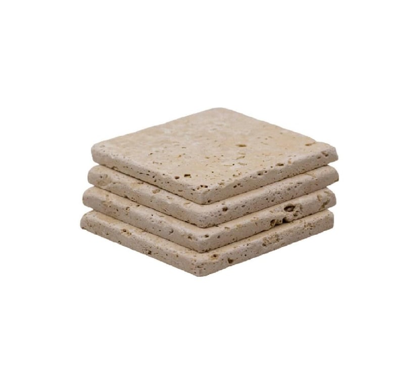 May include: A stack of four square coasters made of light beige stone. The coasters have a textured surface and rounded edges. They are stacked neatly on top of each other, showcasing their natural stone appearance.