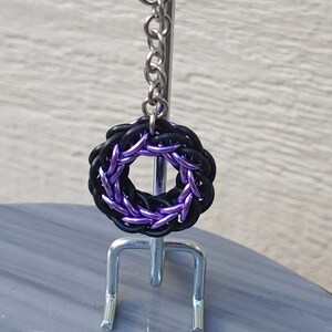May include: A purple and black metal chainmail keychain with a ring attached to a silver chain.