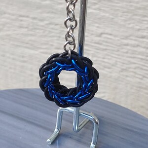 May include: A blue and black chainmail keychain with a silver chain attached to a metal stand.