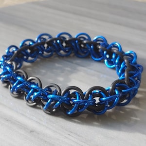 May include: A blue and black chainmail bracelet. The bracelet is made of small metal rings that are linked together in a pattern. The bracelet is a popular style of jewellery for men and women.