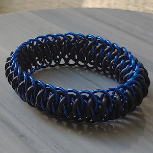 May include: A blue and black chainmail bracelet. The bracelet is made of metal rings that are interlocked to create a flexible and durable design.