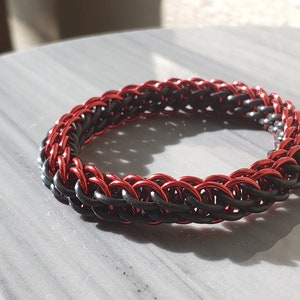 May include: A black and red chainmail bracelet with a woven design.
