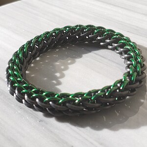 May include: A black and green braided bracelet with a woven design.