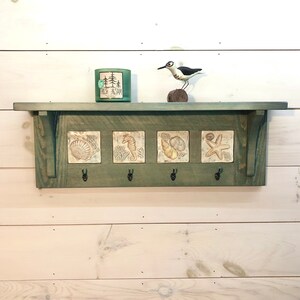 May include: A green wooden shelf with four hooks and three square ceramic tiles featuring sea life designs. The shelf has a small candle on top and a bird figurine.