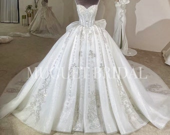 May include: A white strapless wedding dress with a full skirt and a silver glitter design. The dress has a fitted bodice with a sweetheart neckline and a bow at the back.