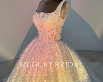 May include: A white wedding dress with a fitted bodice and a full skirt. The dress is covered in intricate lace and beading. The dress is on a mannequin and the background is a light gray.