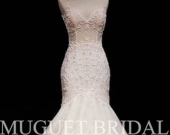 May include: A white mermaid style wedding dress with a lace bodice and a tulle skirt. The dress has a sweetheart neckline and a fitted silhouette. The dress is on a mannequin and the background is black. The text "MUGUET BRIDAL" is visible on the dress.
